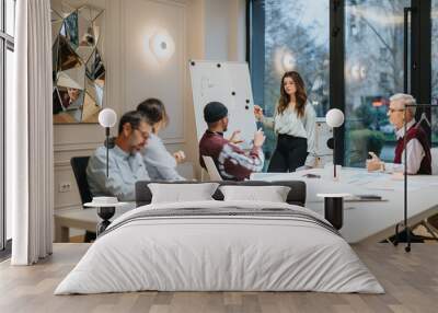 Focused team members in a light-flooded office during a business presentation. The professional atmosphere is clear as a dedicated woman leads the discussion. Wall mural