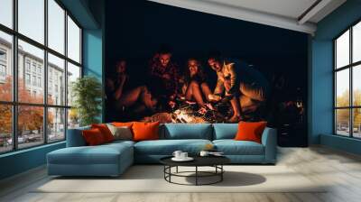 Group of smiling friends sitting near fire on beach Wall mural