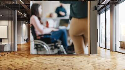 Handicapped female employee in wheelchair collaborating with her colleagues on a project at the office in a pleasant atmosphere. Wall mural