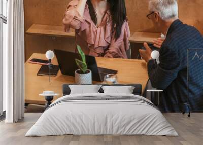 Mature businessman discussing new business plan with his female employee during meeting at the office Wall mural