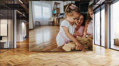 Mom enjoying quality time playing with her two daughters using wooden blocks at home. Family bonding and educational activities. Wall mural