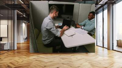 Multiracial male teammates working on their lap tops at modern office and having a conversation Wall mural