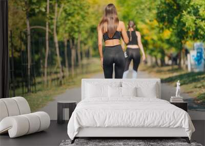 Rearview of two young fit women on roller skates riding outdoors on urban street in the park. Wall mural