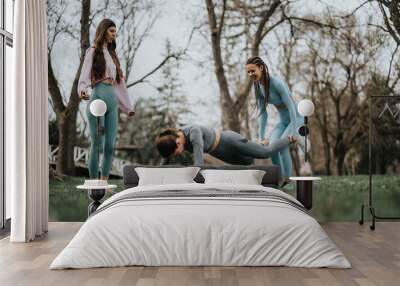 Two athletic women engage in a fitness routine in a serene park setting, demonstrating strength and flexibility. Wall mural