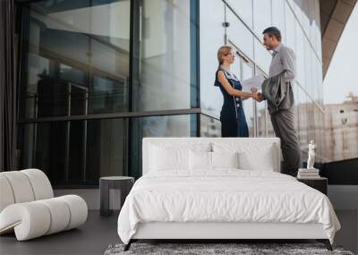 Two business professionals engage in a handshake outside a contemporary glass building, symbolizing agreement and partnership in a corporate setting. Wall mural