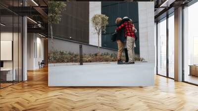 Two professionals in an enthusiastic embrace, celebrating success outside an office setting, illustrating partnership and achievement in business. Wall mural