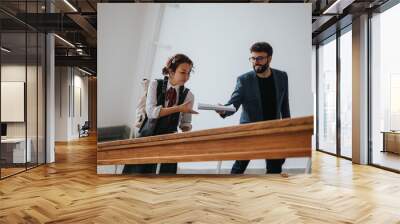 Two students are seen on a staircase, engaging in a friendly exchange of notes, symbolizing collaboration and academic engagement in an educational environment. Wall mural