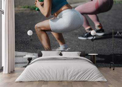 Two women working out in a park, performing squats with dumbbells on a sunny day. Fitness and exercise outdoors. Wall mural