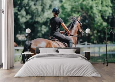 Woman riding a horse in an outdoor equestrian arena, enjoying a sunny day surrounded by nature. Wall mural