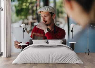 Young business associates discussing documents outdoors in a casual environment. Focused man in red shirt studying papers while his colleague listens attentively. Bright, sunny day enhancing the Wall mural