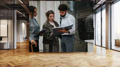 Young business people collaborating on project ideas, discussing strategy and market trends during an outdoor meeting in an urban downtown setting. Wall mural