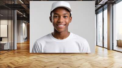 Black teenage boy wearing white t-shirt and white baseball cap isolated on grey background Wall mural