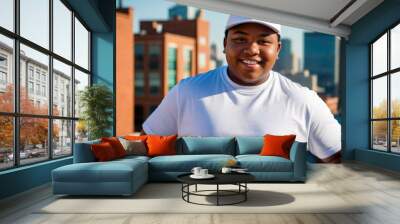 Plus size black teenage boy wearing white t-shirt and white baseball cap standing on cityscape background Wall mural