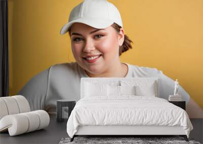 Plus size young woman with short hair wearing white t-shirt and white baseball cap isolated on yellow background Wall mural