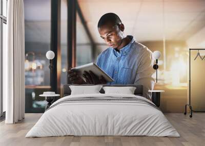 In make things happen mode. Shot of a young businessman using a digital tablet during a late night in a modern office. Wall mural