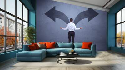 Businessman taking a decision while looking at arrows on the wal Wall mural