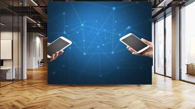 Close up of two hands holding smartphones to each other, wireless connection concept Wall mural