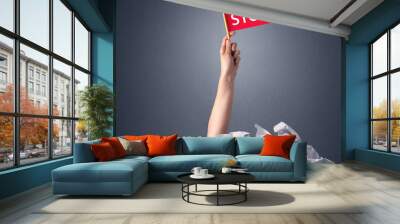 Female hand emerging from crumpled paper pile holding a red flag with stop written on it  Wall mural