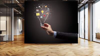 Hand holding light bulb on dark background. New apps concept Wall mural