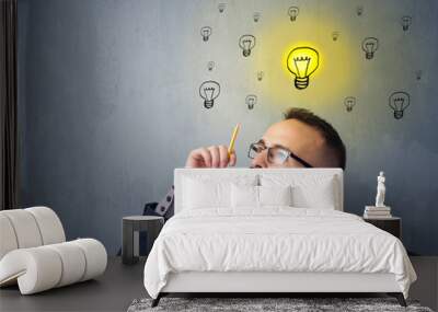 Young businessman sitting behind crumpled paper with lightbulbs above his head Wall mural