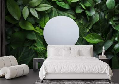 A white circle on a background of green leaves. Wall mural