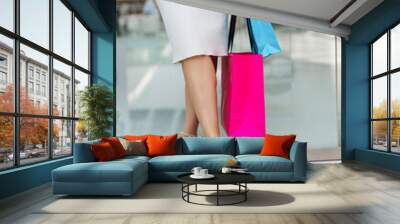 Attractive woman is going to shopping. Beautiful legs of young lady with shopping bags in shopping mall. Buying elegant black shoes on Black Friday. Acquiring new fashionable clothes. Wall mural