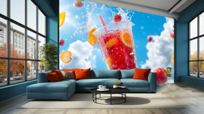 A glass of refreshing iced tea with strawberries and oranges flying through the air with splashes of water against a blue sky. Wall mural