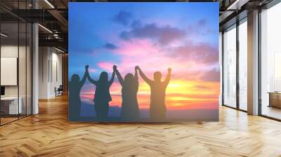 Silhouette of happy business team hold hands up in sunset sky background, business teamwork, business achievement conceptual Wall mural