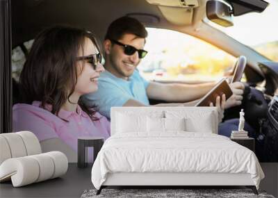 A young woman shows her boyfriend a map in a car while they’re on a trip  Wall mural