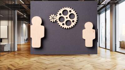 Two gears rotate between two wooden silhouettes of people Concept of teamwork Wall mural