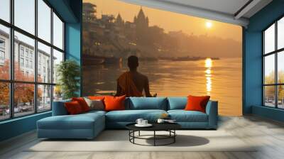 Man meditating at sunrise beside the Ganges in Varanasi, India, reflecting spiritual practices and serene mornings. Wall mural