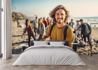 Man volunteer smiling looking at a camera picking up a plastic litter on a beach. Wall mural