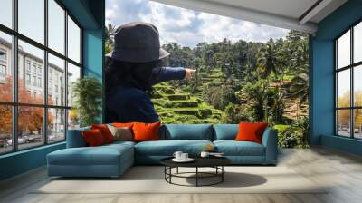 Back view of a female tourist at Tegalalang Rice Terrace in Ubud, Bali. She faces the terraced, green rice fields and tropical landscape under a cloudy sky Wall mural