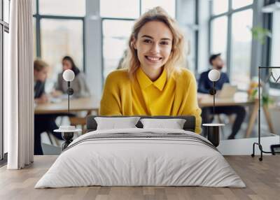 Photo of beautiful happy woman looking at camera while sitting at office Wall mural