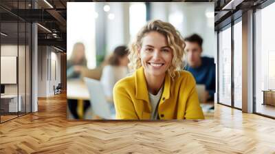 Photo of beautiful happy woman looking at camera while sitting at office Wall mural