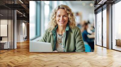 Photo of beautiful happy woman looking at camera while sitting at office Wall mural