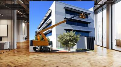 Worker using an  articulated boom lift beside a building exterior Wall mural