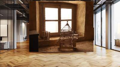 two empty old wooden bird cages in a attic in front of a window Wall mural