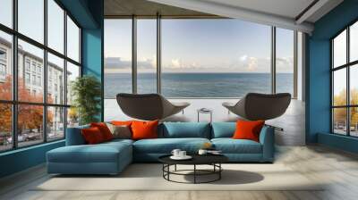 a modern, minimalist interior space featuring two lounge chairs positioned in front of a large glass window. The window offers a panoramic view of the ocean, with calm waters extending to the horizon. Wall mural