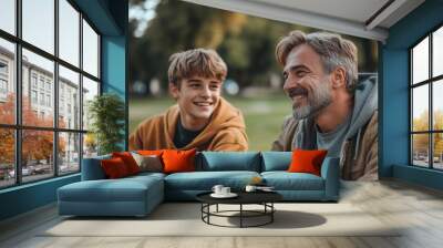 happy father laughing while sitting near teenage son on green lawn in park, Generative AI Wall mural