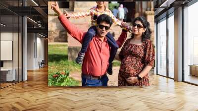 Indian couple posing for maternity baby shoot with their 5 year old kid. The couple is posing in a lawn with green grass and the woman is flaunting her baby bump in Lodhi Garden in New Delhi, India Wall mural