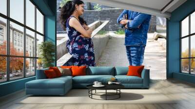 Indian couple posing for maternity baby shoot. The couple is posing in a lawn with green grass and the woman is falunting her baby bump in Lodhi Garden in New Delhi, India Wall mural