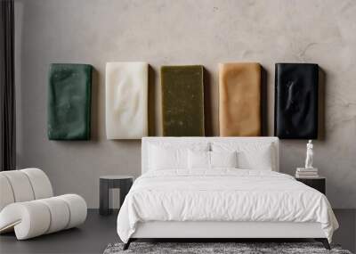 An overhead shot of five rectangular soap bars in various colors green, white, tan, black, and brown arranged in a neat row on a light gray background Wall mural