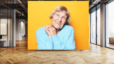 Cheerful old lady in a blue sweater laughs and rejoices on a yellow background. Wall mural