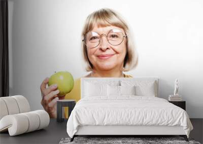 Food, health and old people concept: Portrait of senior woman holding an apple by her mouth Wall mural