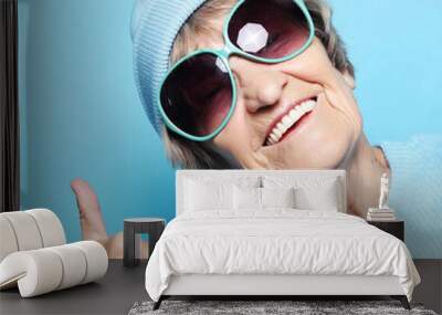 Lifestyle, emotion and people concept: Funny old lady wearing blue sweater, hat and sunglasses showing victory sign. Wall mural