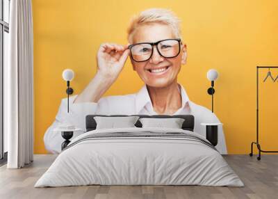 Portrait of smiling mature woman with eyeglasses on yellow background Wall mural