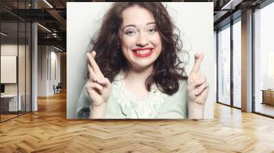 smiley woman hoping hard with fingers crossed against gray backg Wall mural