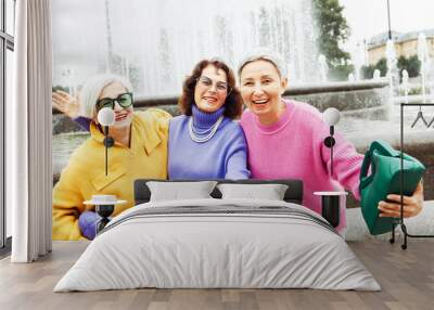 Three happy cheerful pensioner female friends in bright sweaters and sunglasses walk together Wall mural