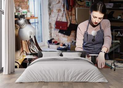 young brunette woman works in a bag making studio, cuts out details Wall mural